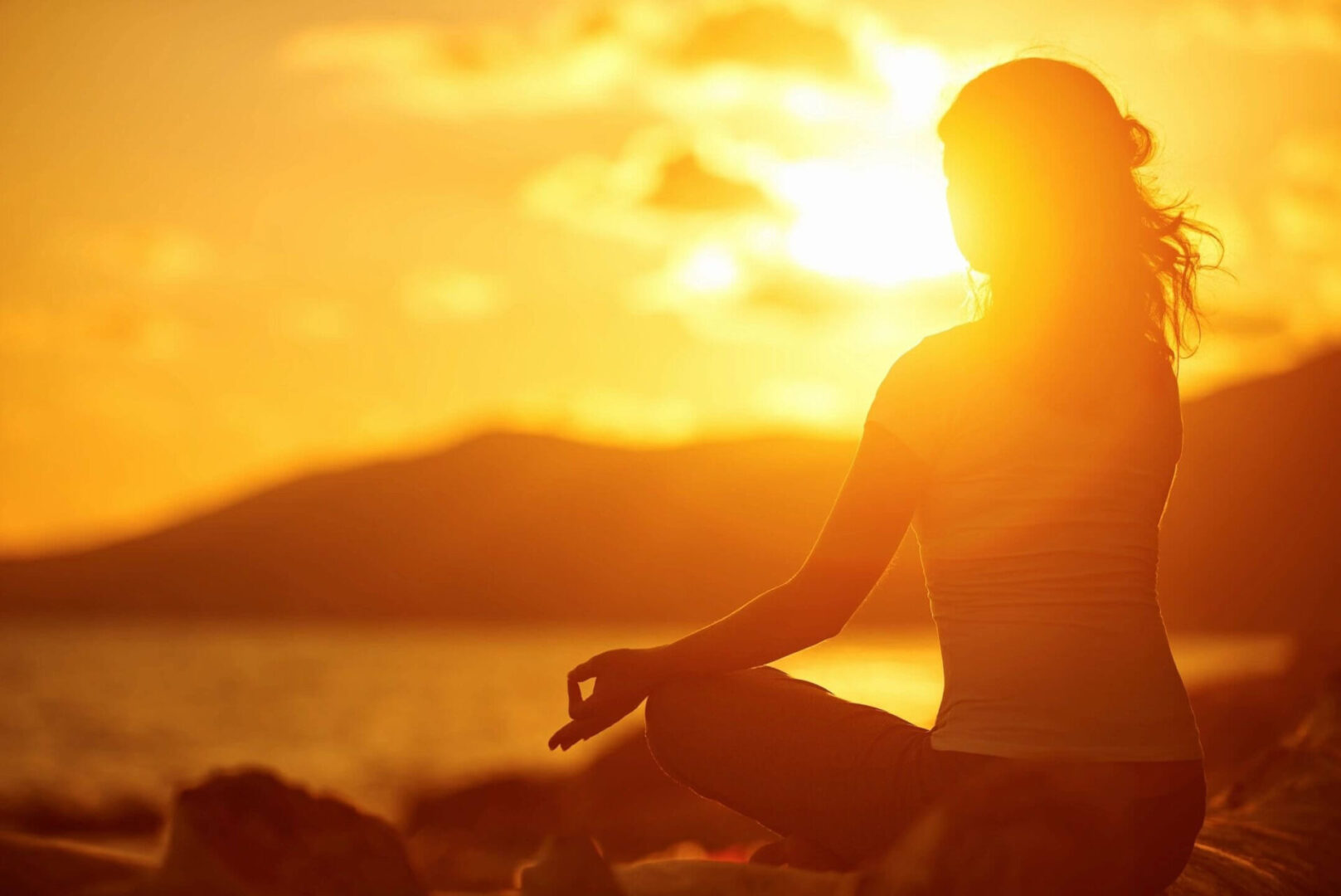 A person sitting in the sunset with their hands in yoga position.