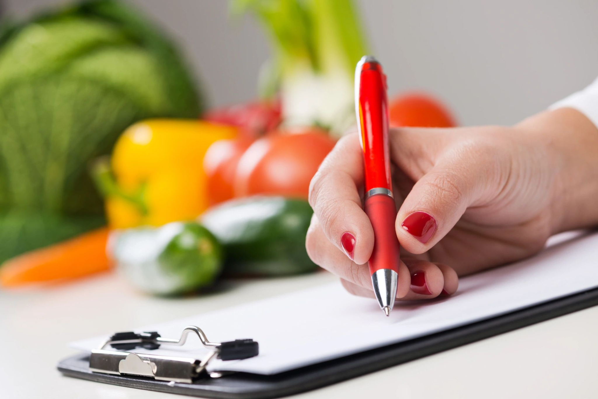 A person writing on paper with vegetables in the background.